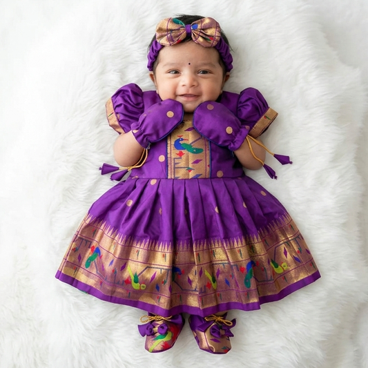 Baby girl wearing purple Paithani newborn frock set with matching mittens and ethnic accessories