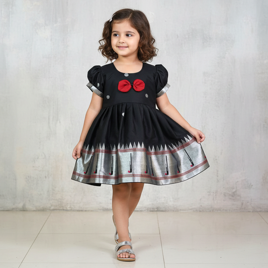 Young girl wearing a black dress with red bows and silver patterns on a light gray background
